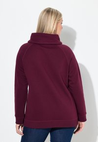Pullover borgogna con collo alto, maniche lunghe a raglan e polsini a coste. Texture morbida, vestibilità rilassata e spacchi laterali all'orlo.