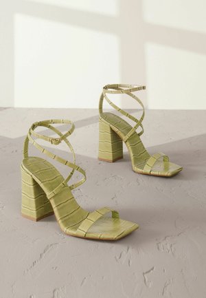 Groene sandalen met hakken, vierkante neus en kruislings banden. Gemaakt van een gestructureerd materiaal dat lijkt op een krokodillenpatroon. Stevige blokhak.