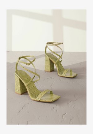 Zöld sarkú szandál négyzettalpakkal és keresztbe tett pántokkal. Krokodilbőr mintázatú, texturált anyagból készült. Vastag blokk sarokkal.