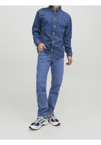 Camisa de mezclilla en azul oscuro, con botones y cuello. Combinada con jeans de mezclilla azul claro. Zapatillas blancas y navy con suela texturizada.