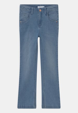 Jean flare en denim bleu clair, avec cinq poches, une braguette zippée avec un bouton en cuivre, et un léger délavage le long des jambes.
