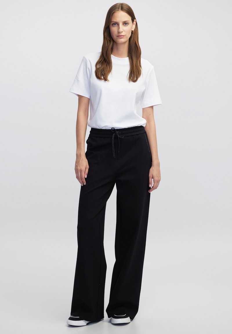 Zwarte wijde broek met een elastische tailleband, gecombineerd met een eenvoudig wit t-shirt met korte mouwen. Glad materiaal met een ontspannende pasvorm.