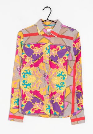 Langærmet skjorte med knapper med barok- og kædemønstre i lilla, gul, pink, beige og turkis, hængende på en sort bøjle.