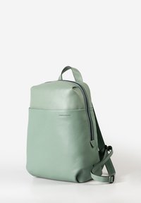 Zaino in pelle verde menta con texture liscia, forma rettangolare, chiusura con zip e spallacci regolabili. Dettaglio della tasca frontale presente.