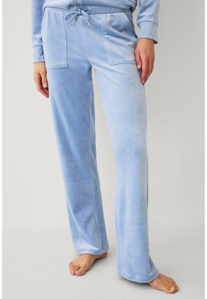 Lichtblauwe velours loungebroek met voorzakken en een taille met trekkoord, gedragen op blote voeten.