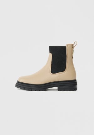 Beige læder Chelsea-støvle med sort elastisk sidepanel, sort robust sål, hæl trækstrop, vist fra siden på en lys baggrund.