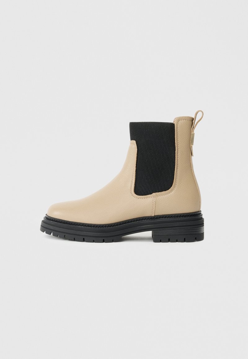 Bottine Chelsea en cuir beige avec empiècement latéral élastique noir, semelle noire épaisse, languette de tirage au talon, vue de côté sur un fond clair.