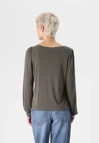 Olive zöld, hosszú ujjú felső, puha anyagból, kerek nyakkivágással és redőzött vállakkal, világos kék farmernadrággal párosítva.
