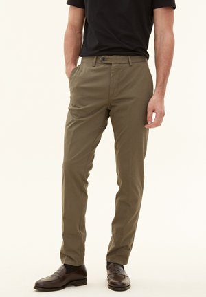 Chinos in cotone verde oliva con vestibilità dritta, dotati di chiusura a bottone, tasche laterali e una texture morbida. Abbinati a scarpe slip-on marroni.