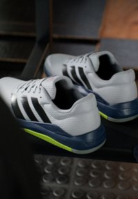 Zapatillas deportivas blancas con rayas negras, parte superior de malla texturizada y suela azul marino acentuada con verde lima. Cuenta con cierre de cordones y cuello acolchado.