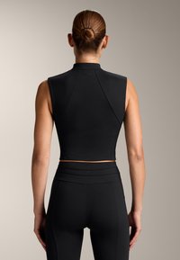 Top corto nero senza maniche con colletto alto, tessuto morbido e design aderente. Abbinato a leggings neri a vita alta.