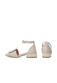 Beige Leder-Sandale mit quadratischer Zehenpartie, verstellbarem Knöchelriemen, ausgestelltem Absatz und einer dekorativen Klappe vorne.