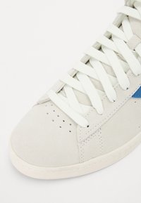 Baskets en daim gris clair avec des lacets blancs, une surface texturée, des perforations et une accent bleu sur le côté. Bout rond et détails cousus.