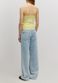 Lichtgele geribde tanktop, gecombineerd met lichtblauwe wijde jeans met achterzakken en een licht vervaagde textuur.