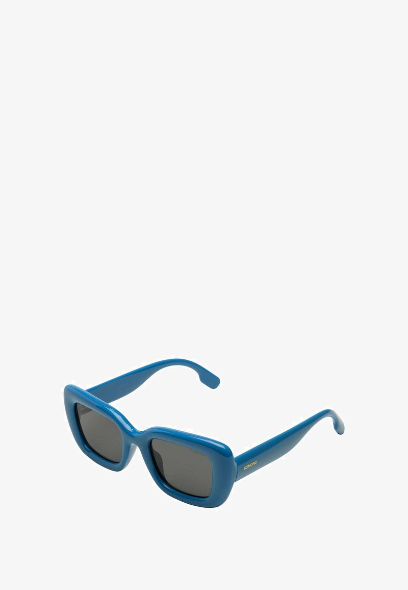 Lunettes de soleil carrées bleues avec des verres opaques et une monture en plastique brillant. Branches fines avec le nom de la marque embossé en or.