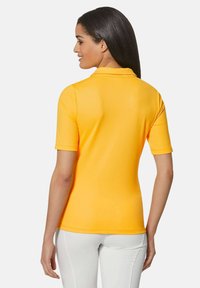 Gele polo met korte mouwen, eenvoudige kraag en een getailleerd ontwerp. Gladde textuur en effen kleur zonder patronen of accenten.