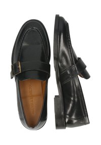 Mocasines de cuero negro con detalle de correa y hebilla, suela plana, punta redondeada, textura suave y forro interior en tono marrón.