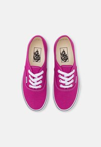 Vaaleanpunaiset kangaskengät, joissa on valkoiset nauhat, matala profiili, kumipohja ja Vans-logo sisäpohjassa.