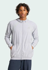 Lichtgrijze hoodie met groene accenten, ritssluiting, elastische manchetten en zijzakken; gemaakt van lichtgewicht, ademend materiaal.
