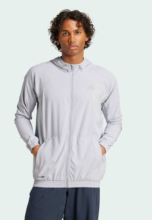 Veste à capuche gris clair avec des accents verts, fermeture zippée, poignets élastiques et poches latérales ; fabriquée en matériau léger et respirant.