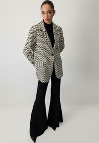 Sacou cu un model geometric alb și negru, având închidere cu un singur nasture, rever și buzunare frontale, asortat cu pantaloni negri evazați.