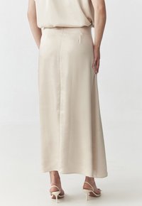 Jupe maxi beige en satin avec une texture lisse, une silhouette droite et un ourlet à la cheville ; dotée d'une fermeture éclair latérale dissimulée.