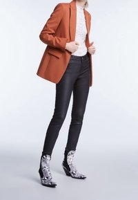 Blazer in ruggine, top in pizzo bianco, jeans skinny neri e stivali alla caviglia con stampa serpente bianca e nera e tacco a zeppa. Vestibilità sartoriale con design strutturato.