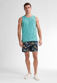 Tyrkysová bezrukávová košile, tmavě modré kraťasy s motivem palmových stromů, bílé tenisky. Volný letní outfit s uvolněným střihem.