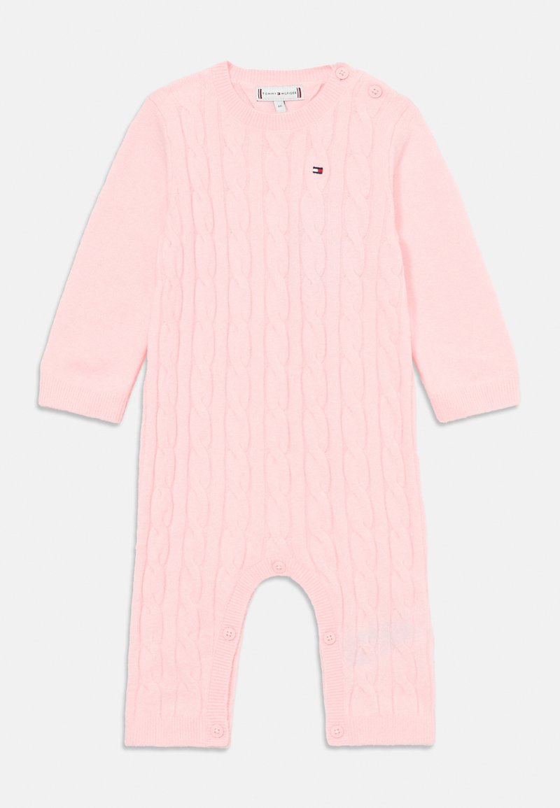 Ružový pletený detský overal s dlhými rukávmi, s gombíkovými uzávermi na pleciach a nohách a malým vyšitým logom na hrudi.