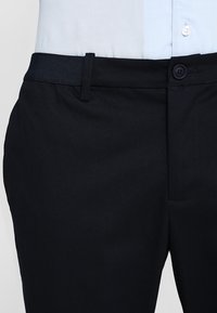 Pantalon bleu marine avec une texture lisse, doté d'une taille texturée, d'une poche avant et d'une fermeture à un bouton.