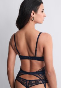 Ensemble de lingerie en satin et dentelle bleu marine avec bretelles réglables, mettant en avant un délicat motif floral et un dos transparent.