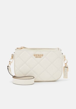 Off-white quilted crossbody bag with gold zipper, detachable strap, and gold "Guess EST 1981" logo and charm.