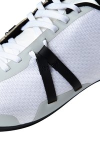 Scarpa sportiva bianca con upper in mesh testurizzato, dettagli neri e lacci bianchi piatti. Presenta una suola in gomma con design a punta arrotondata.