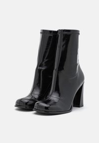 Sorte ankelstøvler i laklæder med høje blokhæle, rundet tå, glat tekstur og diskrete syningsdetaljer.
