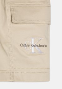 Beżowe szorty cargo wykonane z miękkiego materiału, z wyhaftowanym logo "Calvin Klein Jeans" oraz charakterystycznym wzorem CK na nogawce.