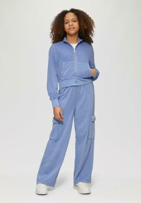Helle blaue Kapuzenjacke mit Reißverschluss und Fronttasche, kombiniert mit passenden weiten Cargo-Hosen mit seitlichen Taschen. Weicher Stoff, lockere Passform.