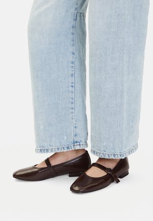 Brązowe baleriny ze skóry z zaokrąglonym noskiem, paskiem i klamrą, zestawione z jasnoniebieskimi jeansami o prostych nogawkach.