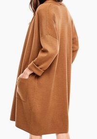 Hnědé oversized šaty vyrobené z měkkého materiálu. Mají kulatý výstřih, dlouhé rukávy a boční kapsu pro přidaný detail.