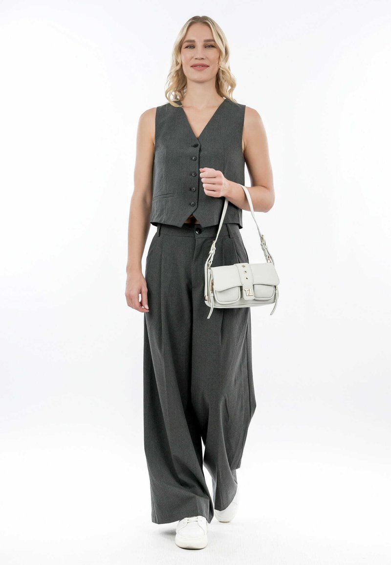 Gilet grigio con bottoni, pantaloni larghi grigi abbinati e scarpe da ginnastica bianche. Borsa bianca con pattina e borchie decorative.