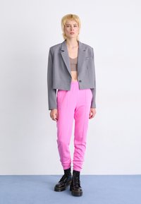 Sivina skrajšana blazer, rjava bralette, roza trenirke, črne čipkaste škornje; gladke teksture, preprost dizajn, kontrastne barve in vidni šivi.