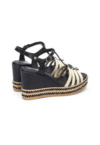 Sandalias de cuña negras y beige con diseño de múltiples tiras, textura tejida y detalles trenzados similares a yute en la plataforma. Cierre con hebilla en el tobillo.