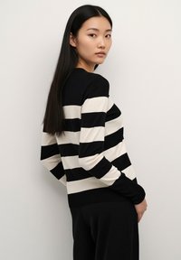 Black and cream striped sweater with long sleeves, round neckline, and ribbed cuffs, made of a soft knit material. Model shown from the side.