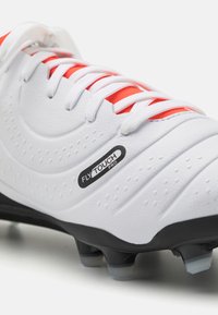 Baltā futbola zābaku ar strukturētu virsmu, sarkaniem un baltiem aukliņām, melnu zoli un FLY TOUCH PRO zīmolu sānos.