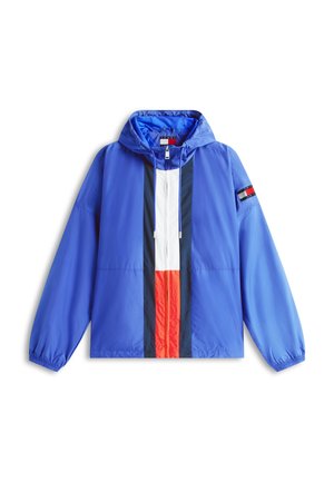 Sinine kapuutsiga tuulejope, mille keskel on valged, punased ja tumesinised vertikaalsed triibud ning vasakul varrukal väike lipuplaat.