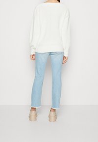 Maglione bianco a maglia con una vestibilità comoda, abbinato a jeans azzurri chiari con orlo sfilacciato e zoccoli color nude con tacco largo.