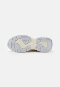 Light-colored sneaker outsole with textured patterns, featuring a combination of gray, white, and rubber textures for traction.