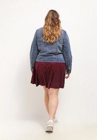 Jeansjacka, utsvängd bordeauxkjol och vita sneakers. Jackan har en klassisk design; kjolen har ett texturerat tyg.