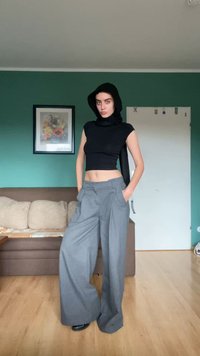 Fekete, testhezálló garbó és szürke, bő szárú nadrág elülső zsebekkel, zöld fal és barna kanapé előtt bemutatva.