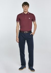 Vínová polo triko s bílými lemy a logem na hrudi. Nosené s námořnickými kalhotami a hnědým páskem, tvořící neformální, sladěný outfit.