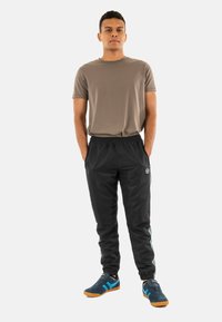 T-shirt grigia a maniche corte, pantaloni jogger neri con vita elasticizzata e dettagli laterali, e sneakers blu con suole arancioni. Sfondo semplice.